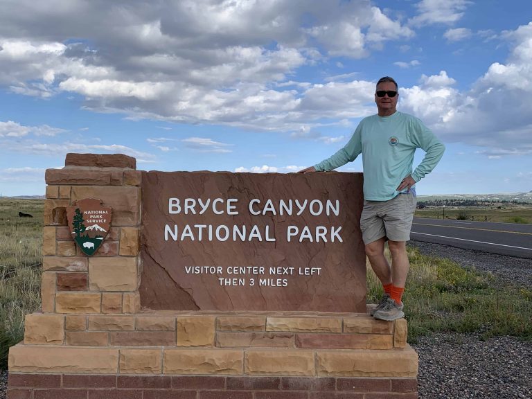 Man standing the the park sign at the entrance to Bryce Canyon National Park