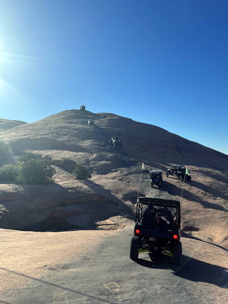 Several 4x4's in a line driving up a large hill in Moab's Hell's Revenge
