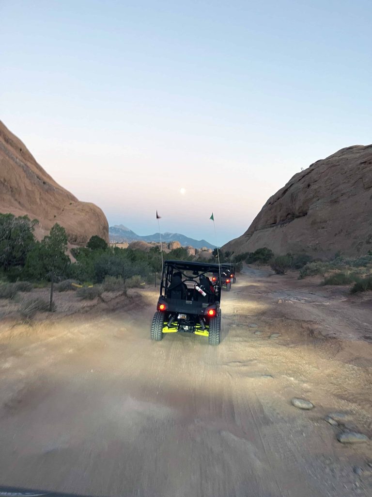 Three 4x4's driving towards the moon and sunset in in Moab's Hell's Revenge