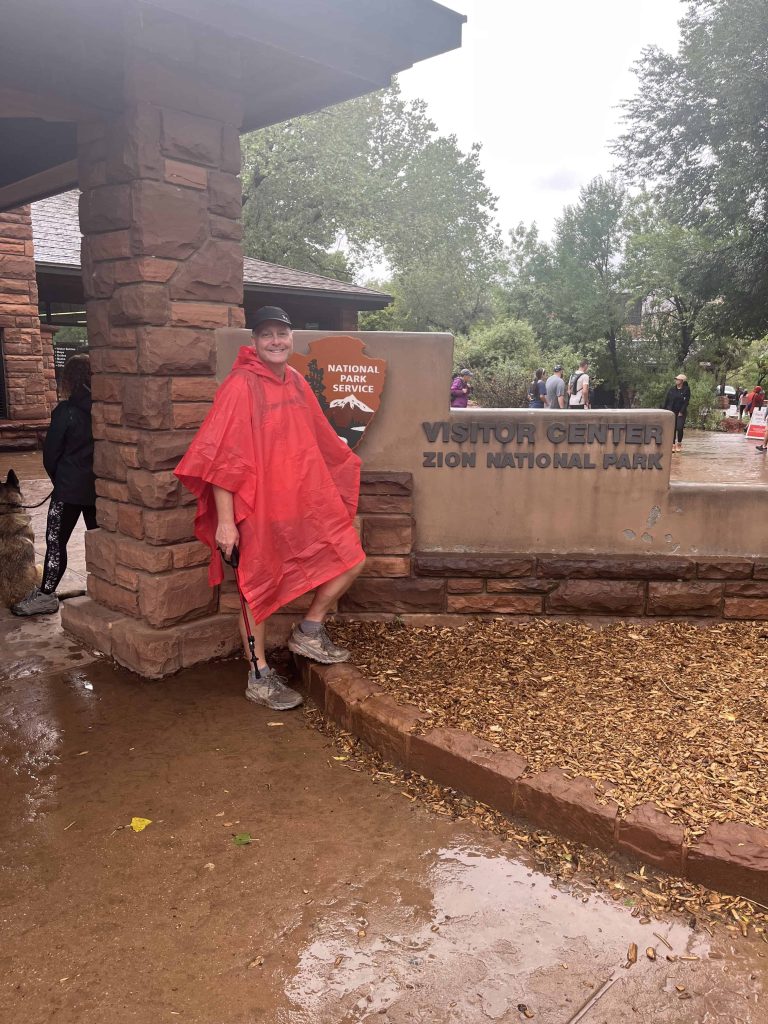 Man in red rain poncho in front of Zion Visitor Sign