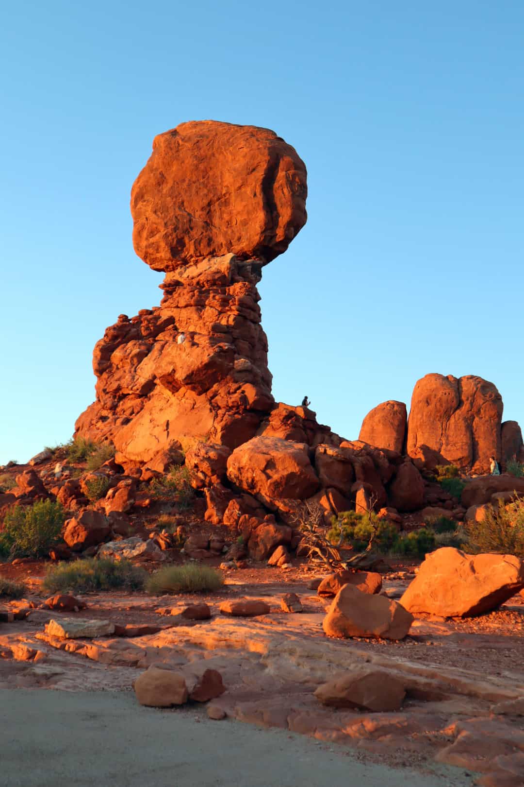 Balance Rock in Arches National Park at sunset with people sitting at base.