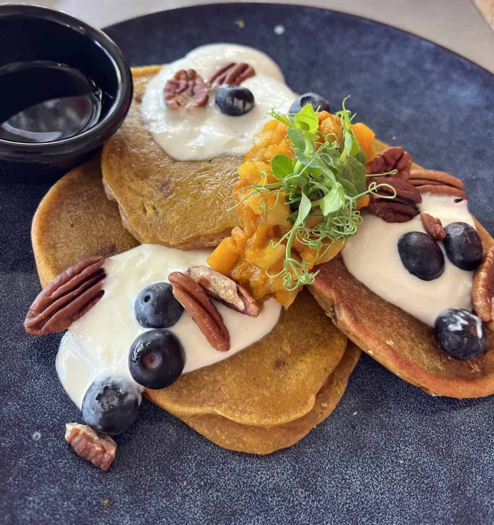A plate with pumpkin pancakes with berries and nuts on top of a cheese drizzle.