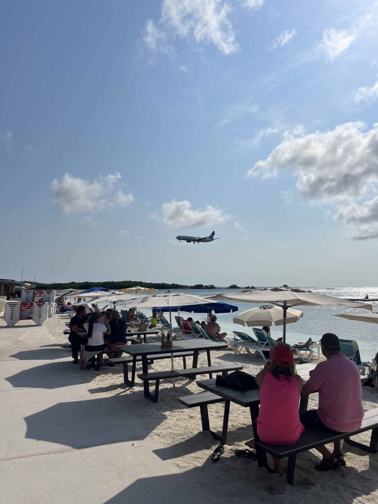 Surfside Bar in Aruba with seating along the beach and plane landing overhead.
